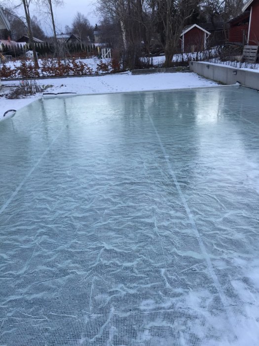 Hemmagjord isrink med pressenning över ram i en trädgård, omgiven av snö.