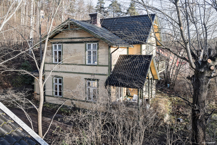 Äldre villa i schweizerstil med flagnande färg och omgivna träd, behov av renovering.