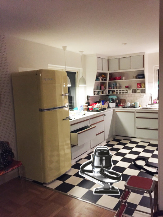Retrostil kök med schackrutigt golv och gul 50-talskylskåp, kompletterat med klassisk dammsugare.