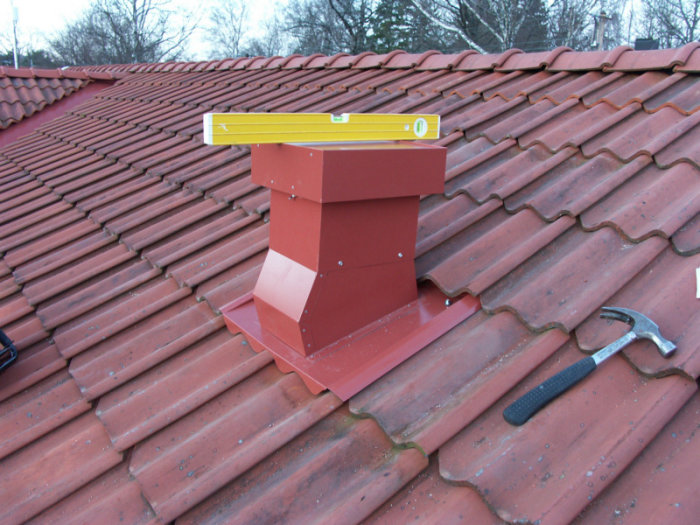 Vattenpass på skorsten på rött tegeltak, verktyg, renovering utomhus.