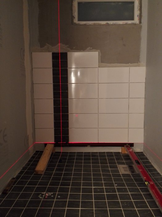 Källardusch under renovering med 10x10 klinker på golvet, 40x20 klinker på väggen och laserlinje för utmätning.
