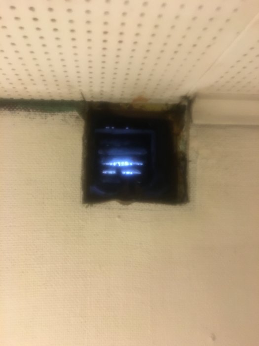 Gulaktigt och fläckigt källartak med öppet ventilationshål som visar gips, svart papp och trästruktur ovanför.