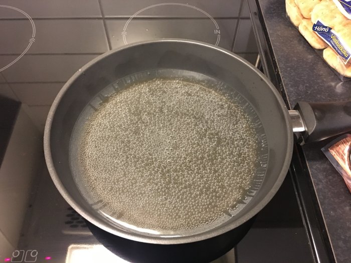 Kastrull på induktionsspishäll fylld med vatten nära kokpunkt, med små bubblor.