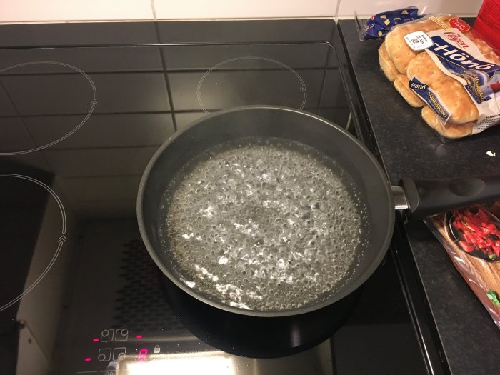 Induktionshäll med en kastrull med kokande vatten, köksmiljö i bakgrunden.