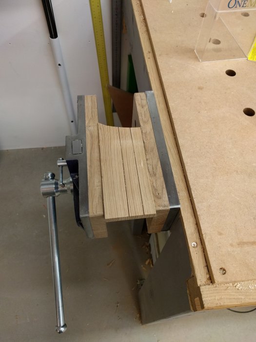 En bit ek trä fastklämd med en skruvstycke visar sågspår och hyvlade ytor efter bearbetning med handverktyg.