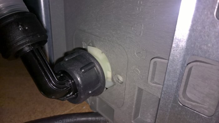 Närbild på vattenanslutningen av en diskmaskin med löst vickande vit plastdel.