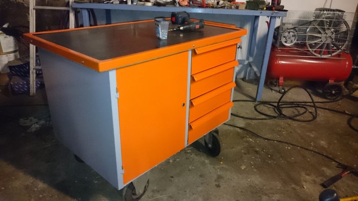 Nyrenoverad grå och orange verktygsvagn med öppna lådor i en verkstadslokal.