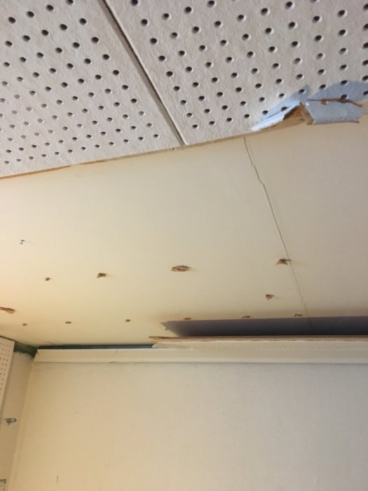 Nedmonterad takbeklädnad som visar spikar och sprickor i underliggande gips.