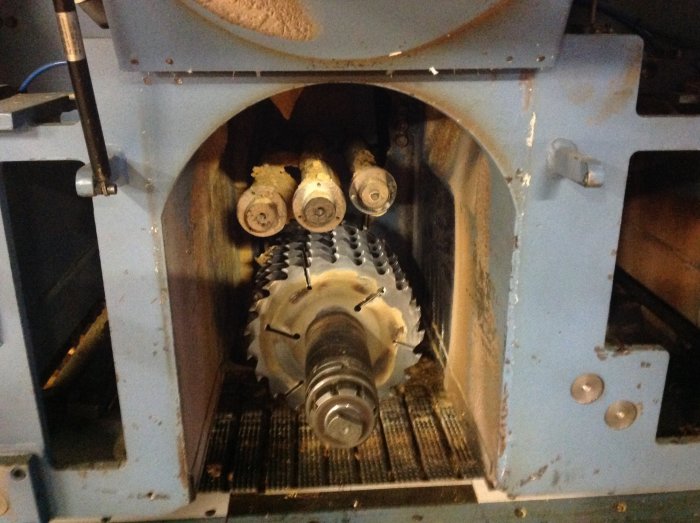 Industrisågmaskin för bearbetning av trä med stora klingor och inmatningsvalsar.