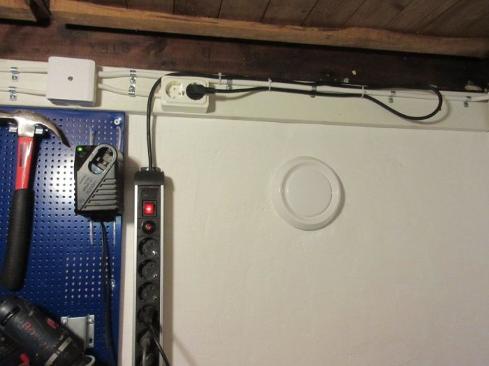 Renoverad ventilinstallation på vit vägg med ny tallriksventil och organiserad kablage ovanför arbetsyta.