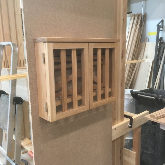 Träpanel med vertikala spjälor monterad på dörr, verktyg och trämaterial i bakgrunden.