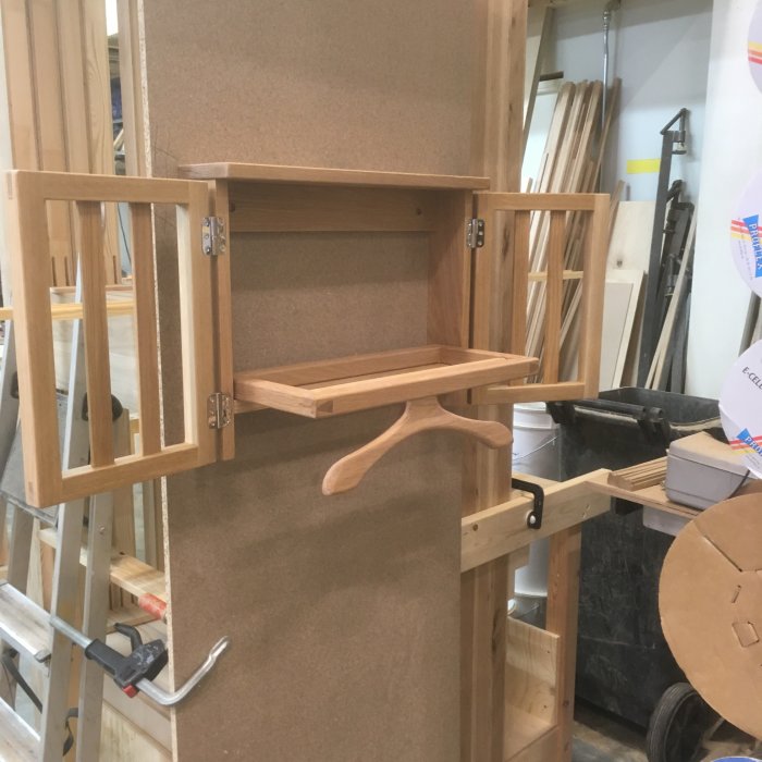En öppen träskåp under konstruktion i en verkstad, med synliga skruvar och verktyg.