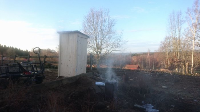 Nybyggd rök som genererar rök, i en uppgrävd trädgård med en skog i bakgrunden.