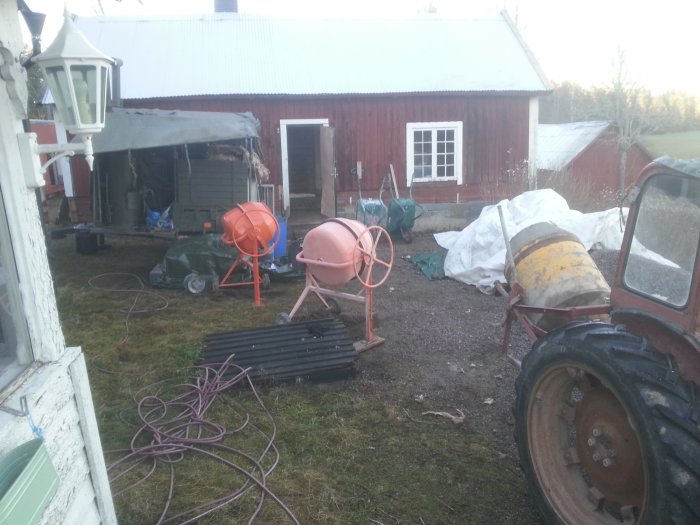 Byggarbetsplats utomhus med blandare, traktor och byggmaterial efter gjutning av betongplatta.