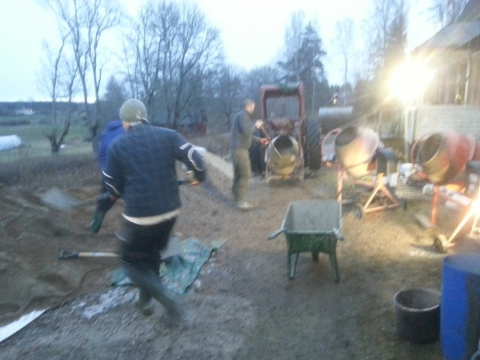 Personer som arbetar med att gjuta en betongplatta utomhus med blandare och skottkärra.