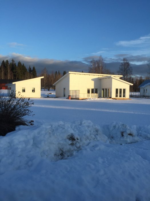 Vita byggnader, snötäckt landskap, klart väder, vintersol, träd i bakgrunden, lugn atmosfär.