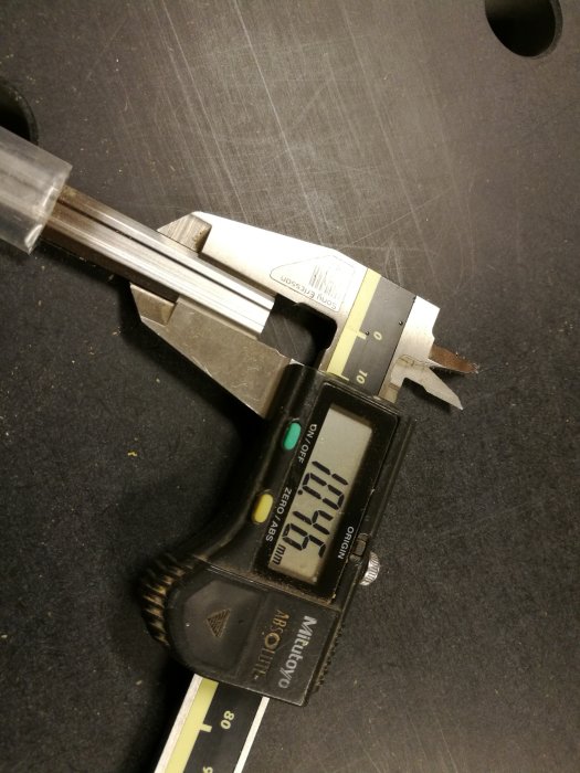 Skjutmått som visar bredden 10.45mm på ett hyvelstål mot en mörk arbetsyta.