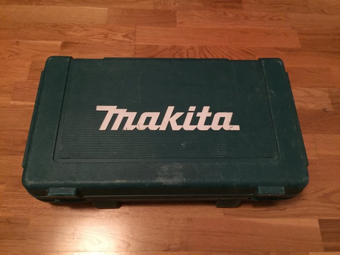 Stängd grön Makita verktygsväska på trägolv, troligtvis innehållande gipsskruvdragare.