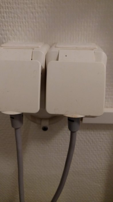 Två vita, slutna eluttag med IP44-klassning monterade på vägg, anslutna med gråa kablar.