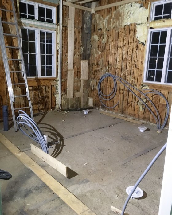 Ett rått och renoveringsklart källarbadrum med avloppsrör i golvet och isoleringsmaterial på väggarna.