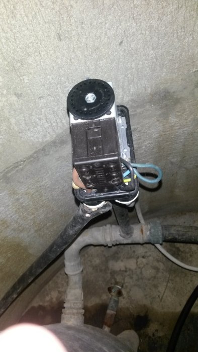 En 1-fas vattenpump med till synes komplicerad elanslutning och flexibla vattenslangar i ett betongrum.