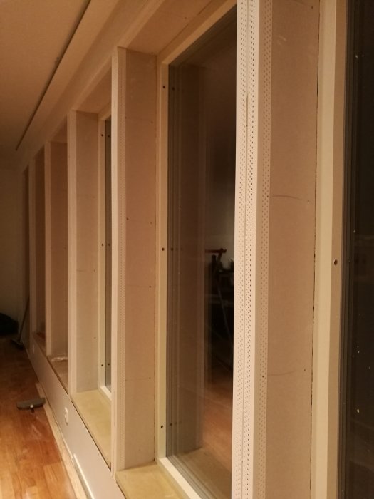 Hög rad av oavslutade fönster med synliga gipshörn och AquaBead förstärkning längs kanterna i ett pågående byggprojekt.