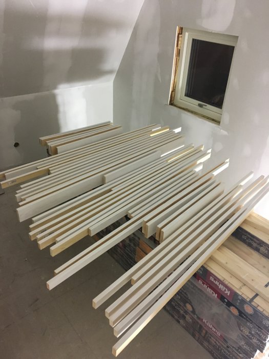 Nytillverkade vita träkonsoler för fönsterbrädor upplagda på ett golv i ett rum under renovering.