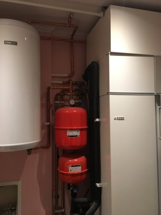 Installation av vit värmepanna med kopparledningar och röda expansionskärl vid sidan om en elpanna.