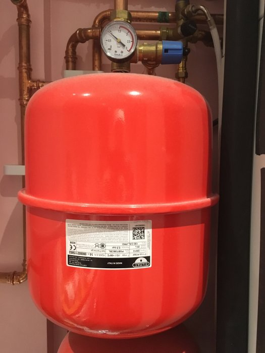 Orange expansionskärl för värmeanläggning med manometer och kopparledningar.