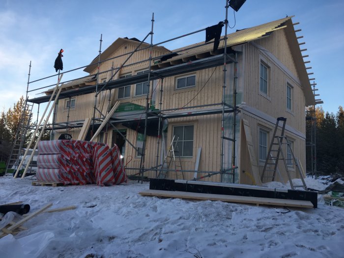 Nybyggt tvåvånings trähus med ställningar och snö på marken under takläggning.