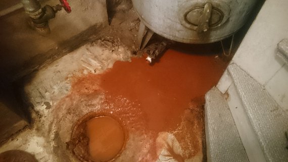 Rostig brun vätska under hydrofor i pannrum, svart PEM-slang och gjutjärnsrör synliga.