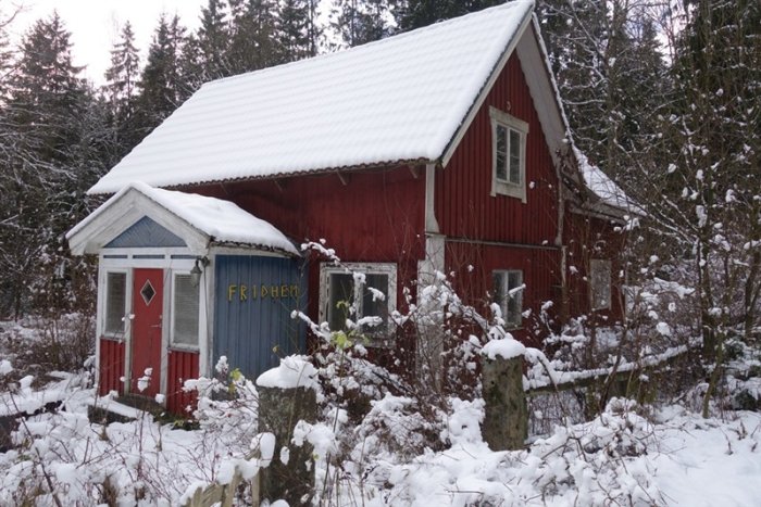 Försummat rött hus med texten "Fridhem" i snöig miljö som visar tecken på behov av omfattande renovering.