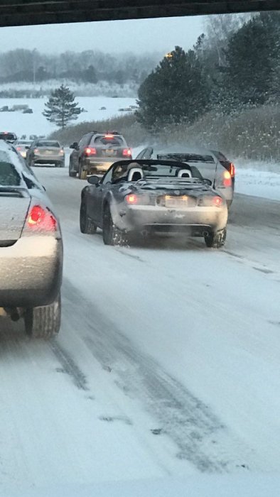 Cabrioletbil med nedfälld sufflett kör på snötäckt väg bland andra bilar i trafik.