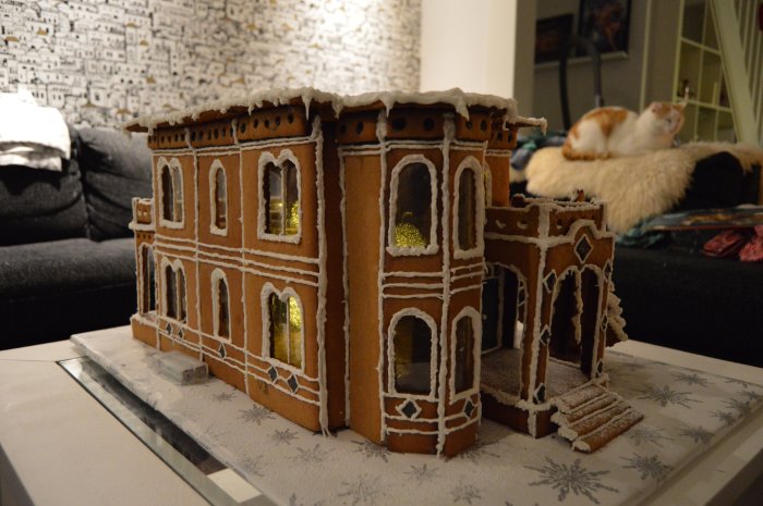 Handgjord pepparkaksversion av ett Victorian house Italianate style, med skumtomte för skala, i ett vardagsrum.