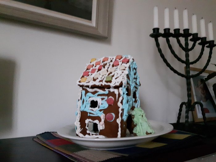 Hemmagjord pepparkakshus med färgglatt godis och glasyr på ett fat framför en menorah.