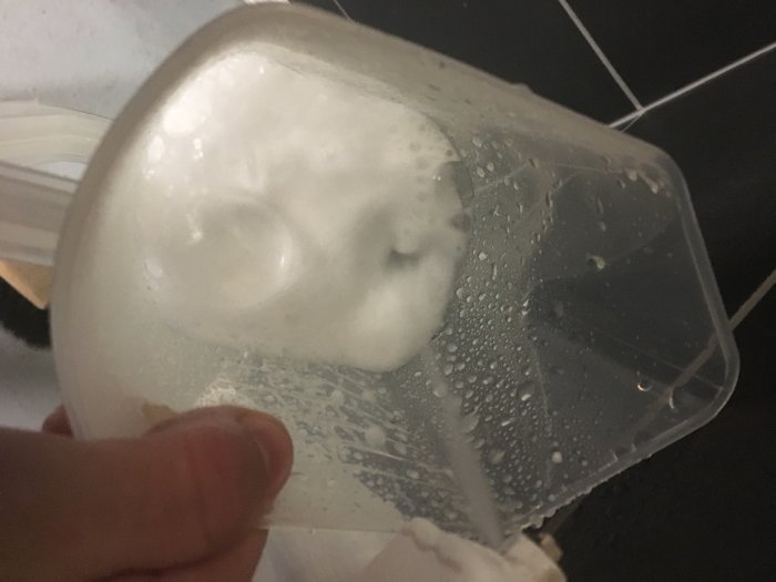 Hand håller en genomskinlig behållare med skummande vitt vatten och kondensdroppar.