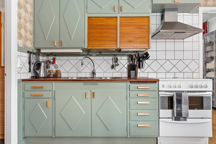 Stämningsfullt kök med gröna luckor, träbänkskiva, vitt kakel och retro handtag.