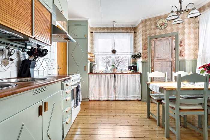 Retrokök med ljusgröna luckor och trädetaljer, pastellfärgad inredning, matbord med stolar och kakeldekor.