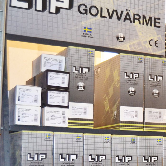 Staplade lådor med LIP golvvärme-produkter framför en stor reklamskylt som marknadsför svensktillverkade värmegolv.