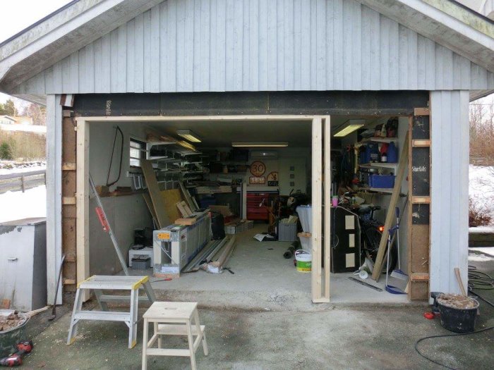 Garage med ryggåstak under renovering, vägg och murad stolpe borttagen för ny portinstallation.