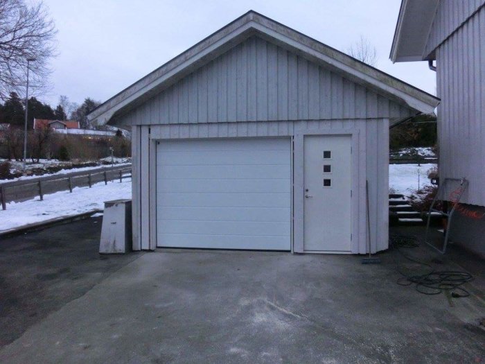 Garage med ny vit port och dörr efter renovering, huset i vinterlandskap.