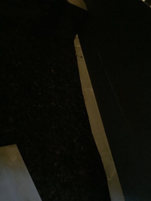 Mörk och suddig bild av ett hörn med mulch och en del av en vit kant vid byggnad.