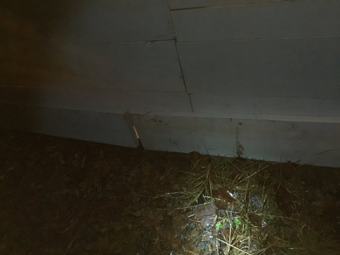 Mörk och suddig bild av en husgrund med synliga skador och en utstickande spik.