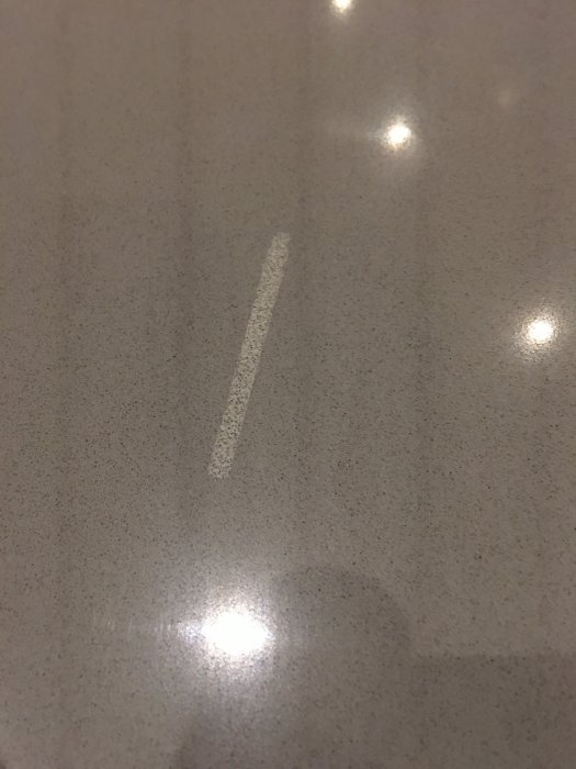 Skadat område på silestone-bänkskiva, rektangulärt och ljusare i färg, skrovligt jämfört med den omgivande polerade ytan.