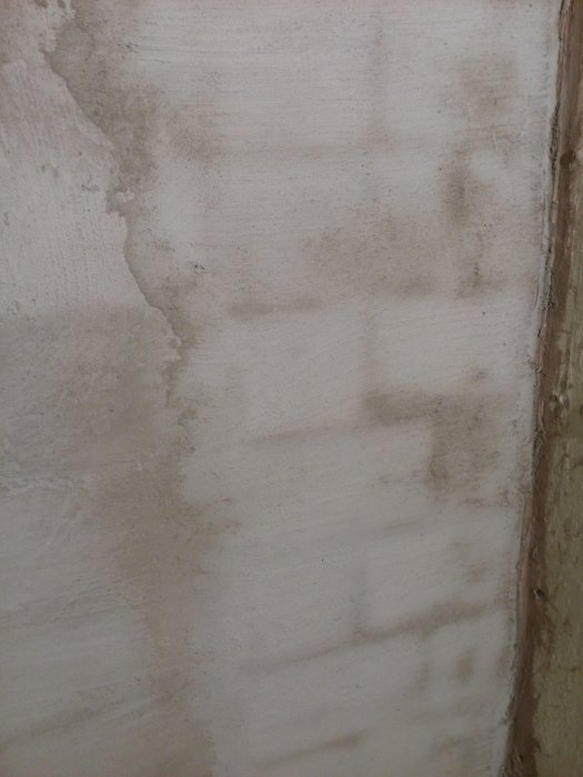 Vägg med ojämn puts och mögelspår, behov av renovering eller behandling.
