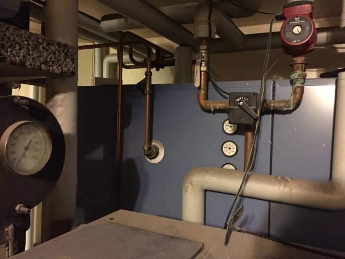 Värmesystem med rör, manometer, termostat och en cirkulationspump i ett pannrum.