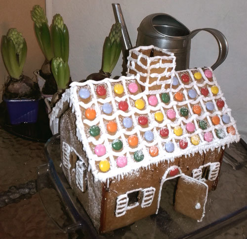 Pepparkakshus med färgglada godisdekorationer på vedspis i äldre hus.