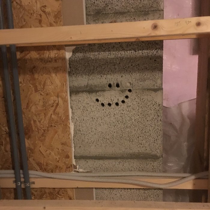 Inre väggar under konstruktion med synliga träreglar, isoleringsmaterial och en betongvägg med hål för elinstallationer.