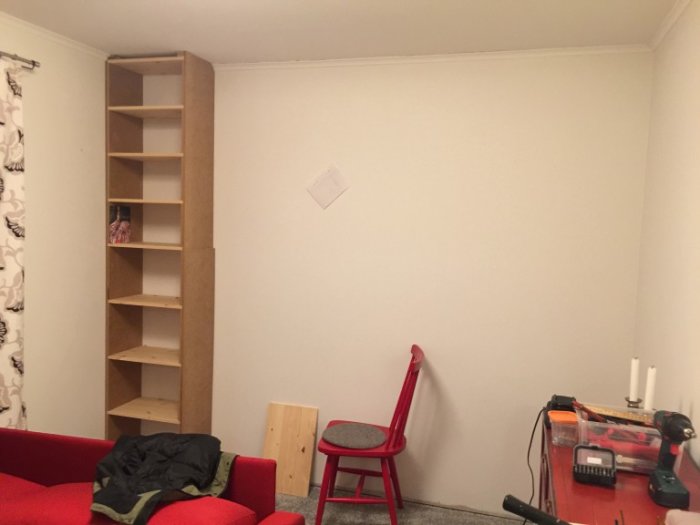 Högt, obehandlat bokhyllprojekt av MDF och furuhyllplan från golv till tak i ett vardagsrum under konstruktion.