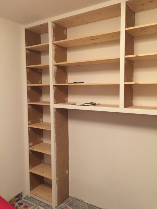 Nybyggd bokhylla av MDF och furuhyllplan som sträcker sig från golv till tak utan böcker.